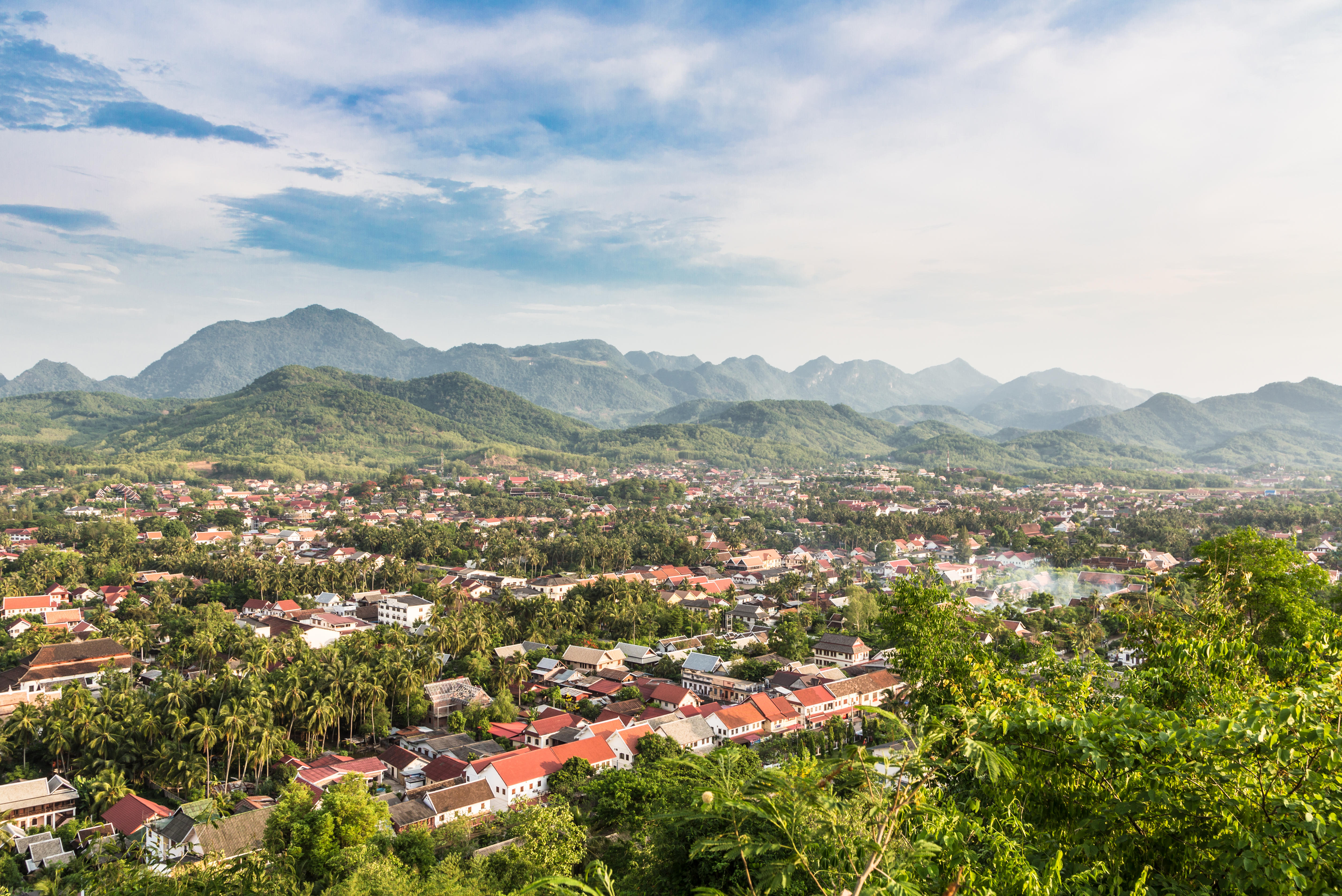 Aerial view of Luang Prabang, Laos, showing the city nestled among palm trees with mountains in the background.