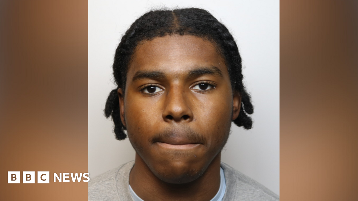 Young 18 year old man sits in the passenger seat of a black VW car, his arm resting on the open window as he looks to camera