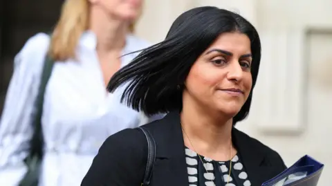 PA Media Shabana Mahmood, with hair flying in the wind, clutches a blue folder in Downing Street