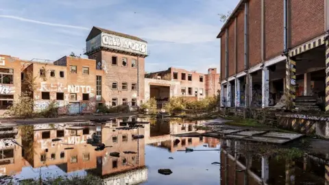 Capital&Centric Old industrial brick buildings. The land between two separate blocks is muddy and water covers the floor, reflecting the buildings in it.
