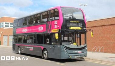 A dark grey double decker bus with a pink banner with West Midlands branding