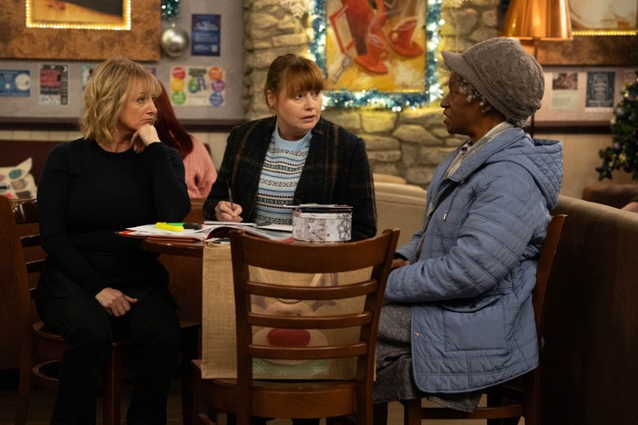 Claudette, Nicola and Lydia sit around a table in the cafe with documents in front of them in Emmerdale