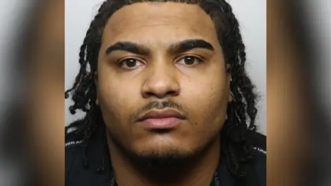 Avon and Somerset Police A police mugshot of Talbert Young, wearing a black t-shirt with his hair in shoulder-length braids. 