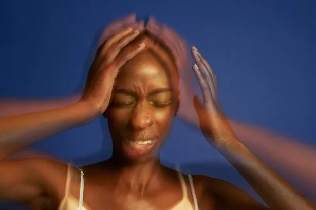 Multiple exposure of frustrated young woman with autism holding head in hands with eyes closed against blue background