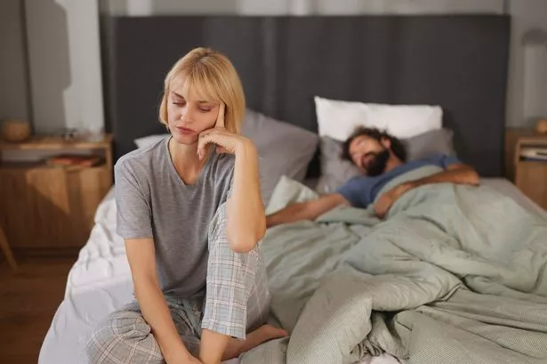 A woman sitting on the edge of the bed, lookiing unhappy