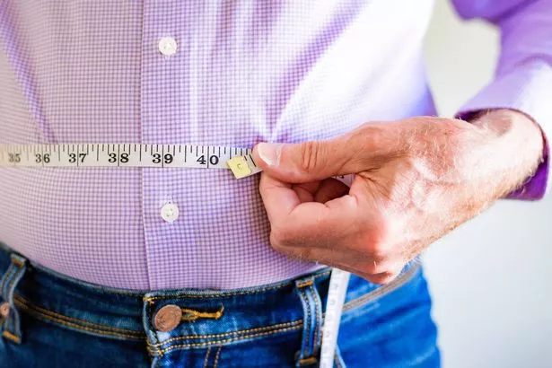 Close up color image depicting a senior man measuring his waistline with a tape measure.