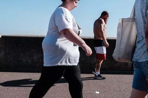 Clacton on Sea, UK - September 14th, 2020: Two men and a woman busily walking by the seaside with cloudless blue sky in late summer afternoon.