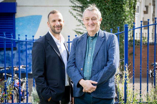 Two men in front of a bright blue fence
