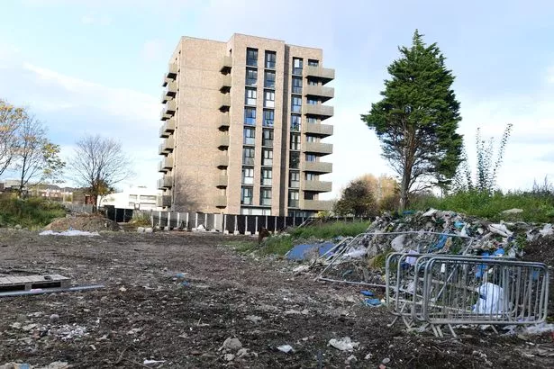 A modern high rise building in the background while the foreground shows wasteland reminiscent of a post apocalyptic TV show 