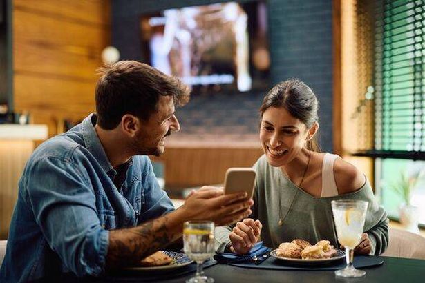 Young happy couple using cell phone during their meal in restaurant.