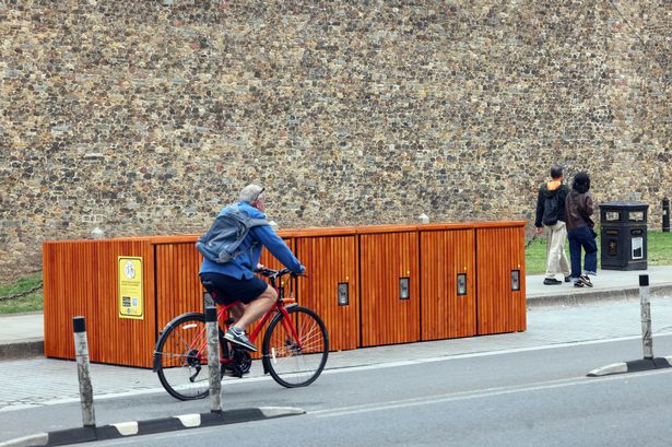 A cyclist riding past some bike lockers