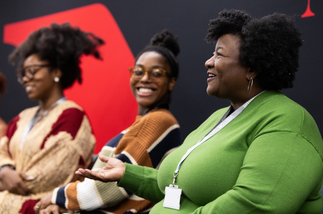 Three attendees laughing and talking in front of a Northeastern London backdrop during the Black History Month event.