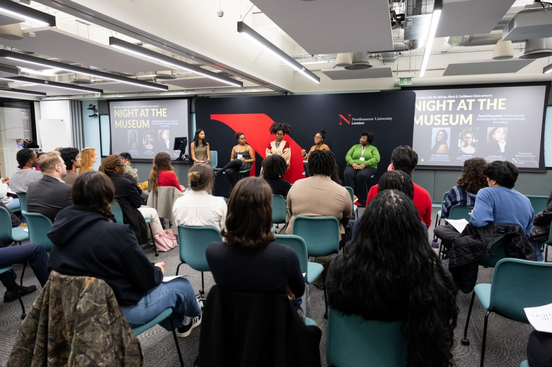 A group of five people stand sit and present between two projectors at Northeastern University London’s “Night at the Museum” event celebrating Black History Month.