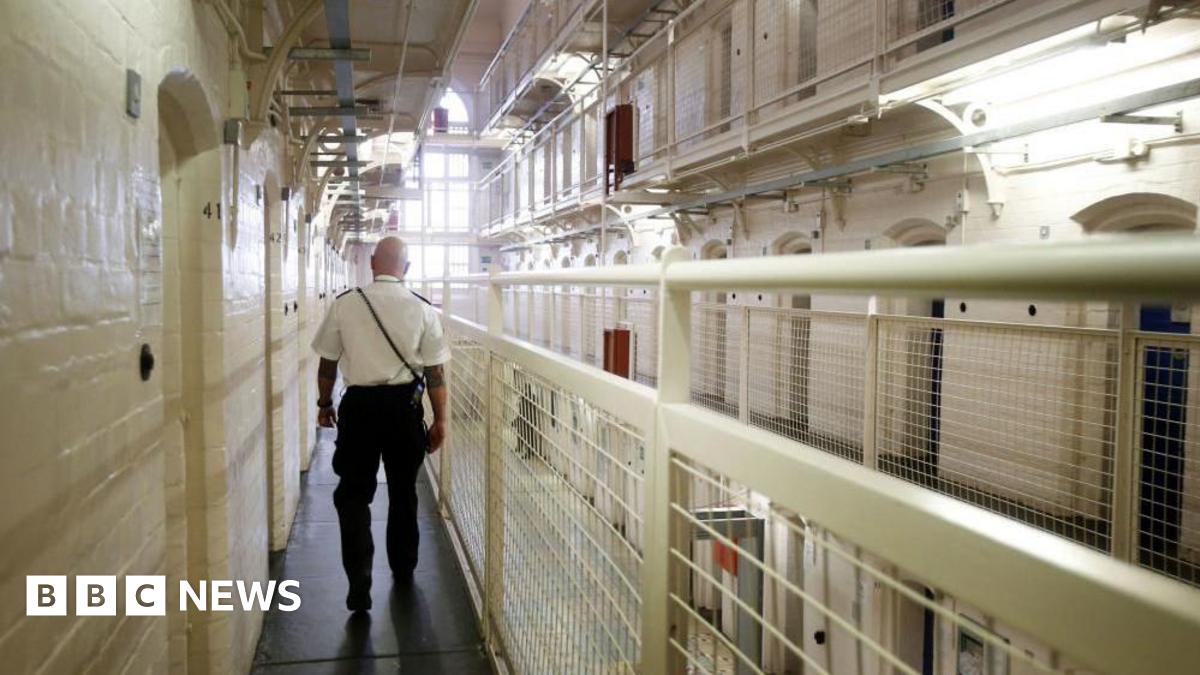 A man in uniform walks down a landing of prison cells.