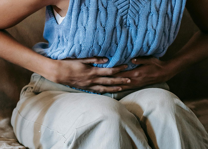 Person wearing a blue sweater sitting and holding their stomach, illustrating a moment from psychiatric institution workers' unforgettable experiences.
