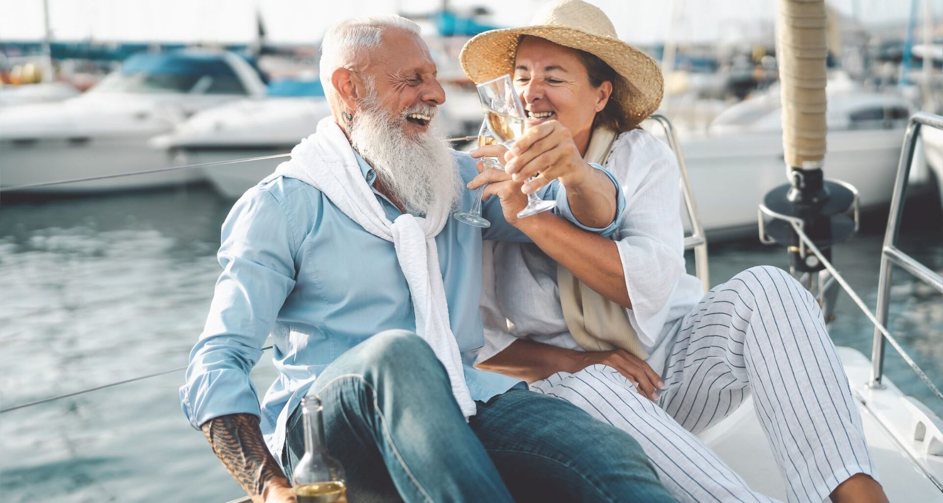 Senior couple toasting champagne on sailboat vacation - Happy elderly people having fun celebrating wedding anniversary on boat trip - Love relationship and travel lifestyle concept.