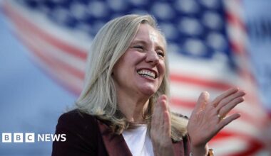Spanberger smiles and holds out a hand. There's a US flag in the background