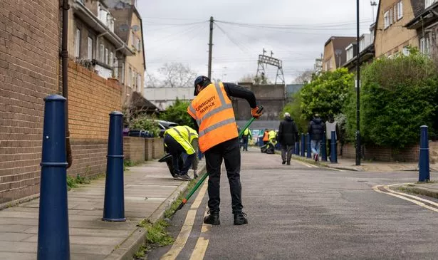 A man on Community Payback uses a hoe to clear weeds from a street in Bethnal Green