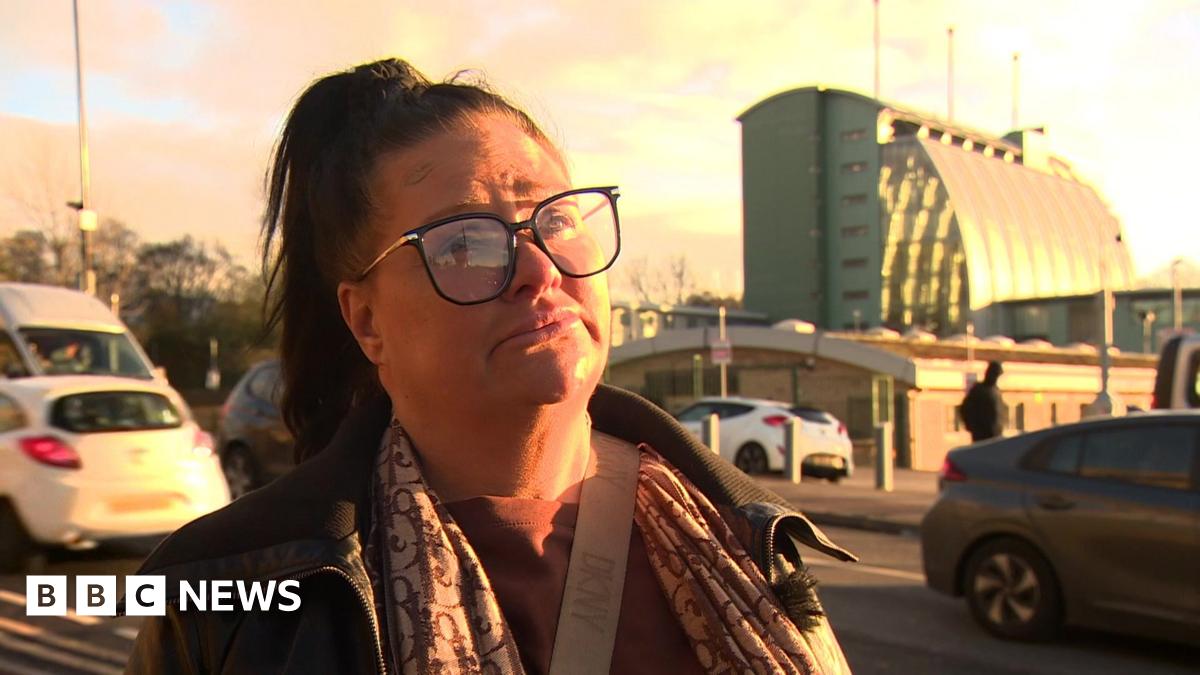 Caroline Willgoose, who has dark hair tied up in a ponytail and black rimmed glasses. She wears a neutral expression while listening to an interviewer's question.