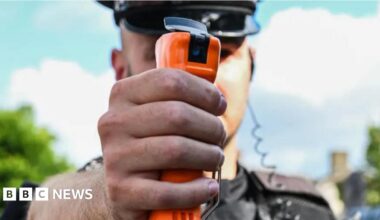A close-up of an orange-coloured DNA spray container in the outstretched hand of a police officer.