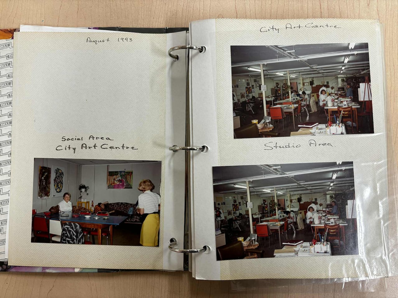 Three pictures in a photo album dated August 1993. One photo shows people sitting in a lounge area, the other two show artists working in an art studio with tables and canvases.