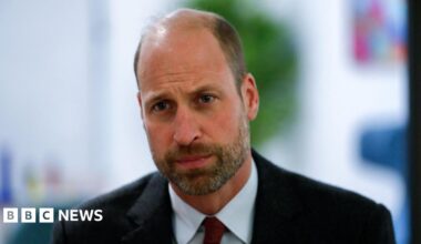 The Prince of Wales wearing a black blazer, blue shirt and red tie.