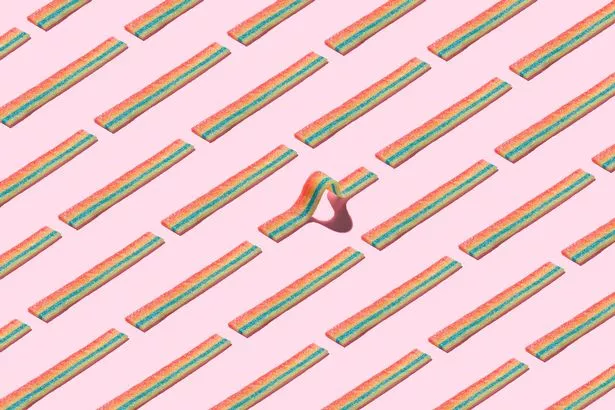 A Curved Rainbow Striped Candy Standing Out Form the Crowd on Solid Pink Colored Background.