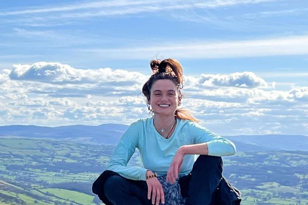 The image shows Ellie, young looking with brown hair and fair skin, posing on top of a mountain