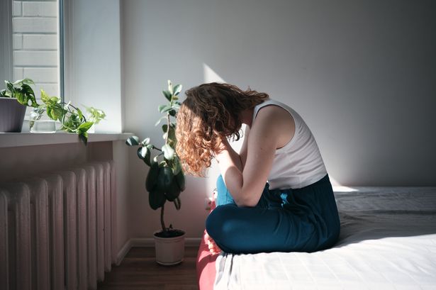 Depressed woman sitting on bed holding head in hands, waking up with depression. Sad anxious female sitting on bed holding head in hands suffering from headache