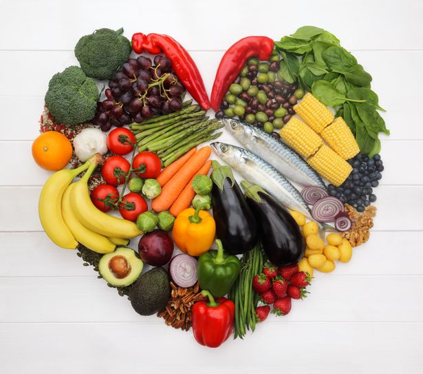 Healthy foods, which make up part of a Mediterranean diet, arranged to create a heart-shape, mackerel (fish), Ramiro peppers, bell peppers, tomatoes, nocellara and leccino olives, asparagus, carrots brussel sprouts, aubergines, red onions, avocados, green beans, spinach, corn, brocolli, potatoes, garlic, strawberries, blueberries, red grapes, bananas, orange, pecan nuts, walnuts, pumpkin seeds and mixed seeds.