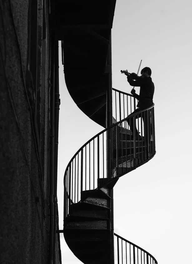 A man plays a violin on a staircase. An image from Gary Williamson's photography collection Through Their Lens