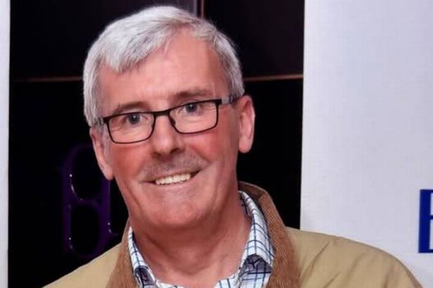 A man with white hair and rectangular glasses