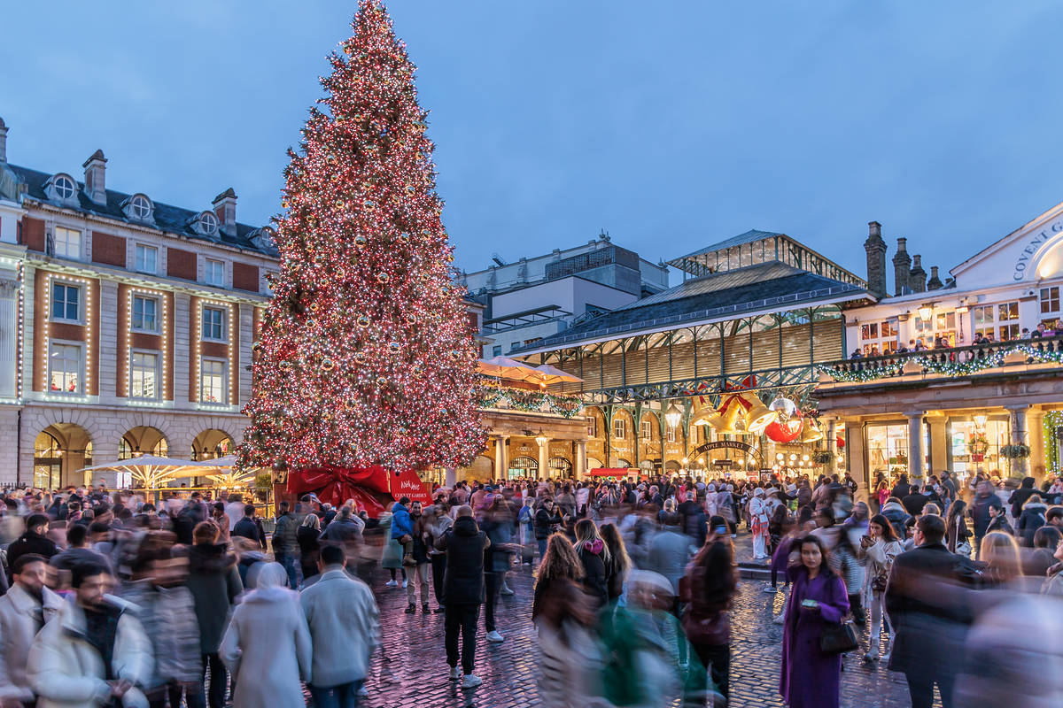 a christmas tree towering over covent garden at dusk, with hundreds of people milling about enjoying the christmas decorations