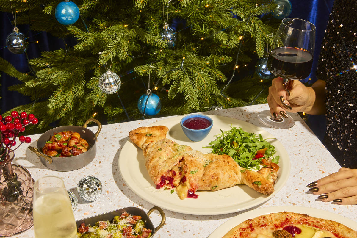 a christmas calzone on a plate on a table with side dishes and a glass of wine scattered around it