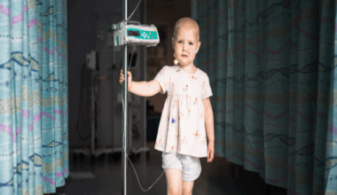 A photo of a little girl standing in the camera, she is wearing shorts and a top and holding onto a machine.