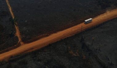 A an overhead drone photo of a bus driving along the Transamazon Highway as it passes through deforested and burnt land.