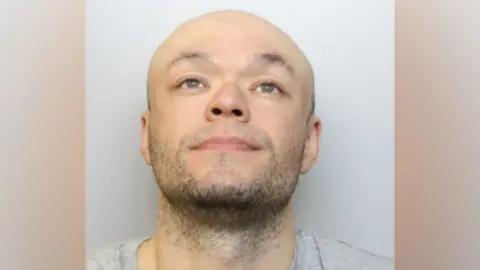 Avon and Somerset Police Jamie Doyle custody image. He is wearing a grey T-shirt and is looking up into the air.