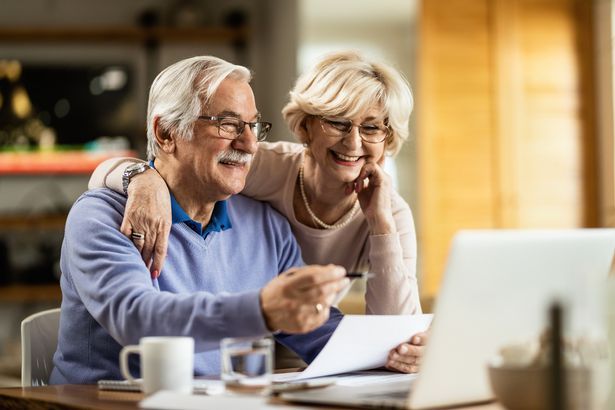 A man and woman are sitting looking at a computer screen smiling 