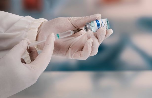A young doctor in a white protective glove holds a medical syringe and a vial