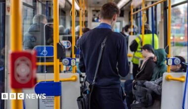 A tram conductor in a navy blue uniform with short dark hair is collecting fares from passengers