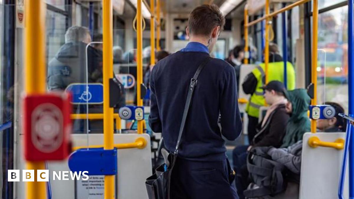 A tram conductor in a navy blue uniform with short dark hair is collecting fares from passengers