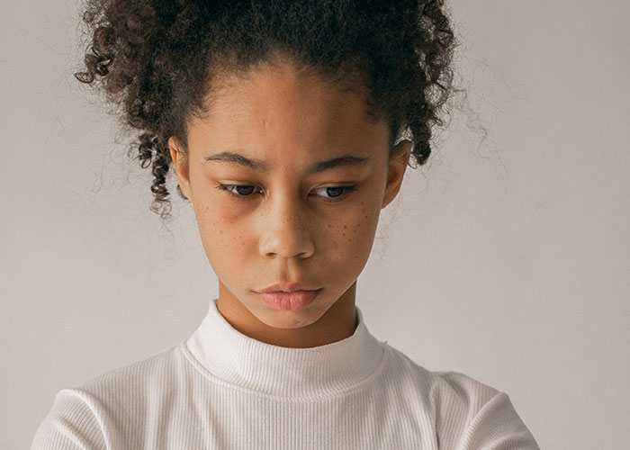 Young woman with curly hair wearing a white top, appearing thoughtful, related to psychiatric institution workers experiences.