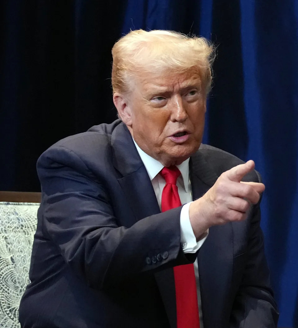 President Donald Trump seated, gesturing with one finger raised