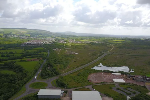 An aerial view of land where housing is being built near a settlement and a road