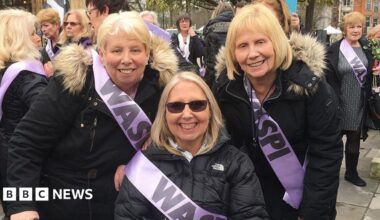 Sisters (left to right) Mary Waterhouse, Norma Elkington and Susan Dutton wearing black coats and lilac sashes with 'Waspi' written on them at a campaign rally
