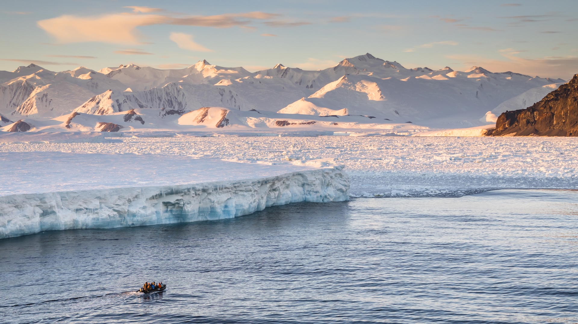 ice shelf and icy Antarctic mountains in sound with small boat in foreground