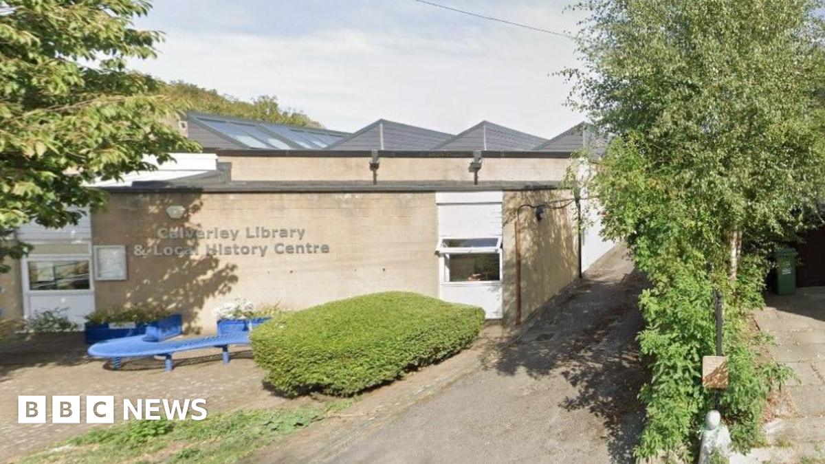 A single-storey, cream-coloured stone building, with a paved area to the front where there is a blue 'S'-shaped bench.