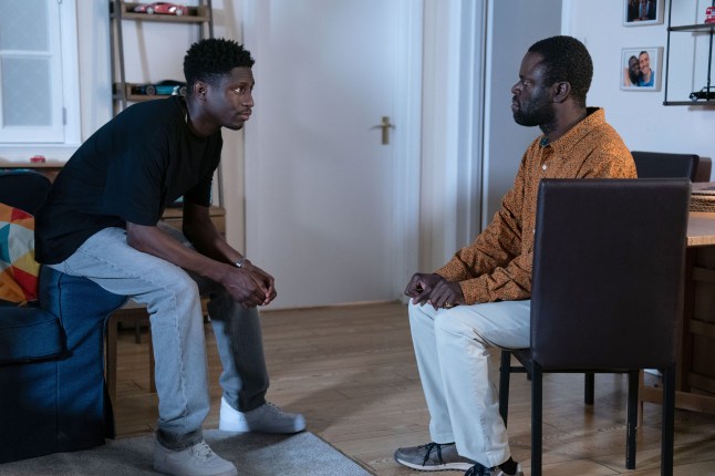 Okie sitting across from Kojo in his flat in EastEnders