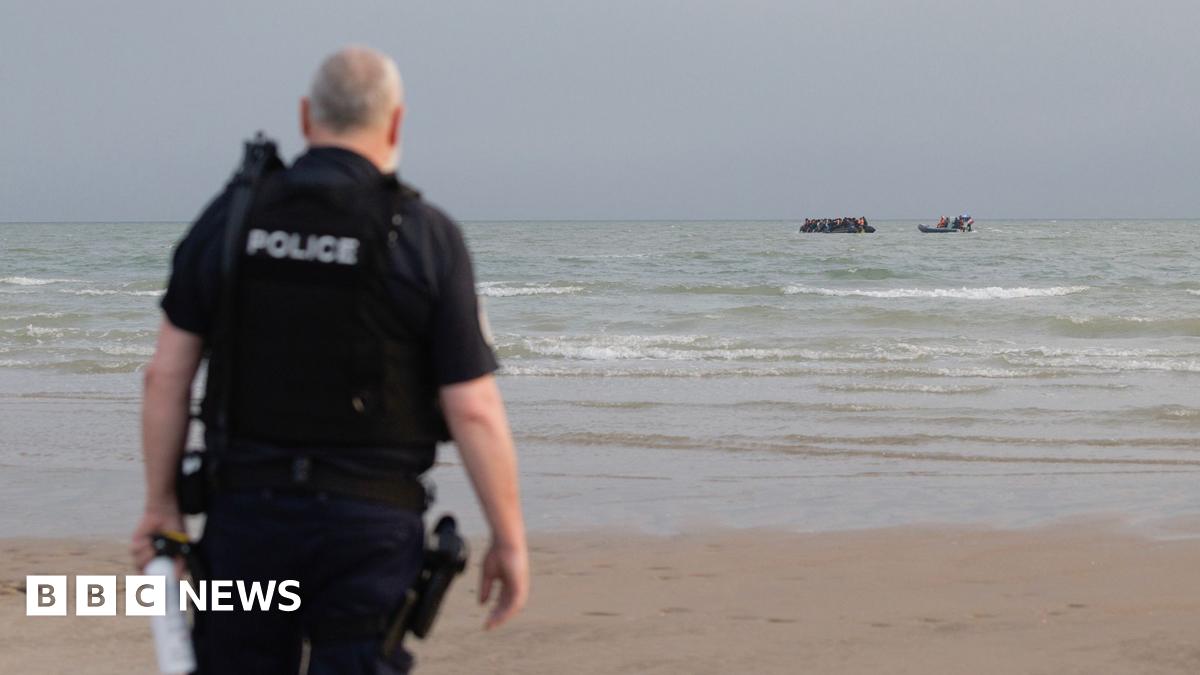 A French police officer stands on the beach at Gravelines as a French maritime police rib approaches a small boat off the coast in the background, taken in July.