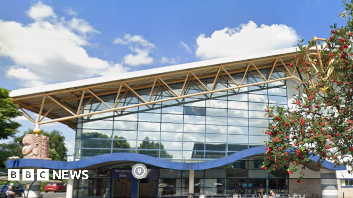 A large interior room with a wooden floor and walls in grey, beige and green. A row of black cross trainers runs from one end of the room to the other